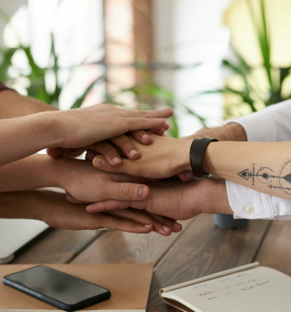 Hands from a diverse team stack on a table symbolizing unity and teamwork in a modern office setting.
