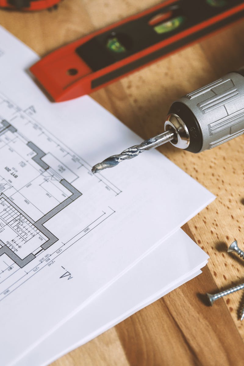 Close-up of construction blueprint with tools like drill and screws on a wooden table.